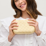 Woman holding a woven beige clutch against a white background