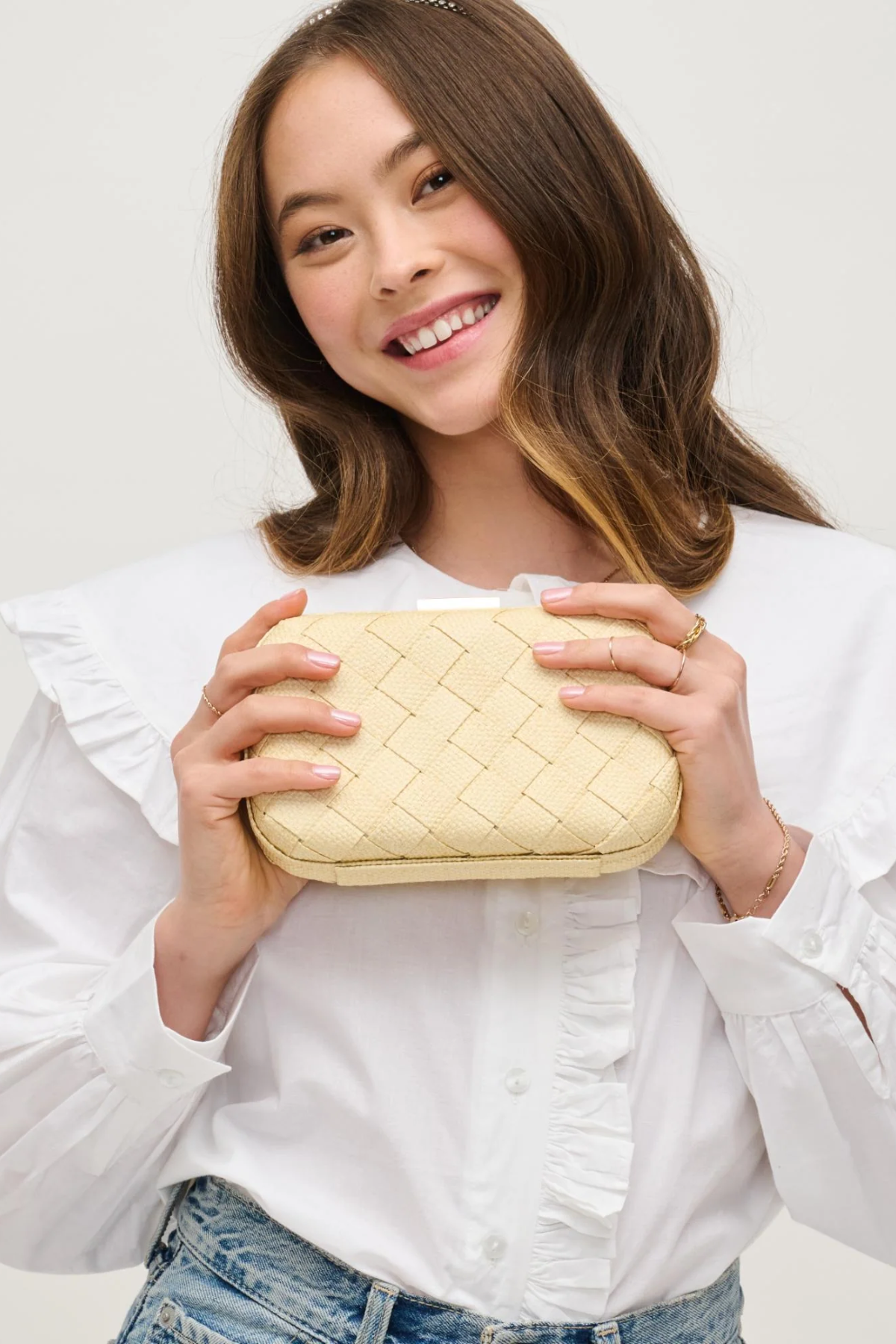 Woman holding a woven beige clutch against a white background