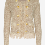 A cropped, long-sleeve tweed jacket in a textured champagne beige with gold buttons and fringe detailing, shown against a plain light gray background.