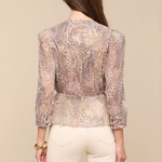 Woman wearing a patterned blouse and white pants on a beige background