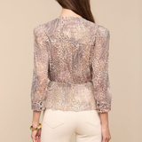 Woman wearing a patterned blouse and white pants on a beige background