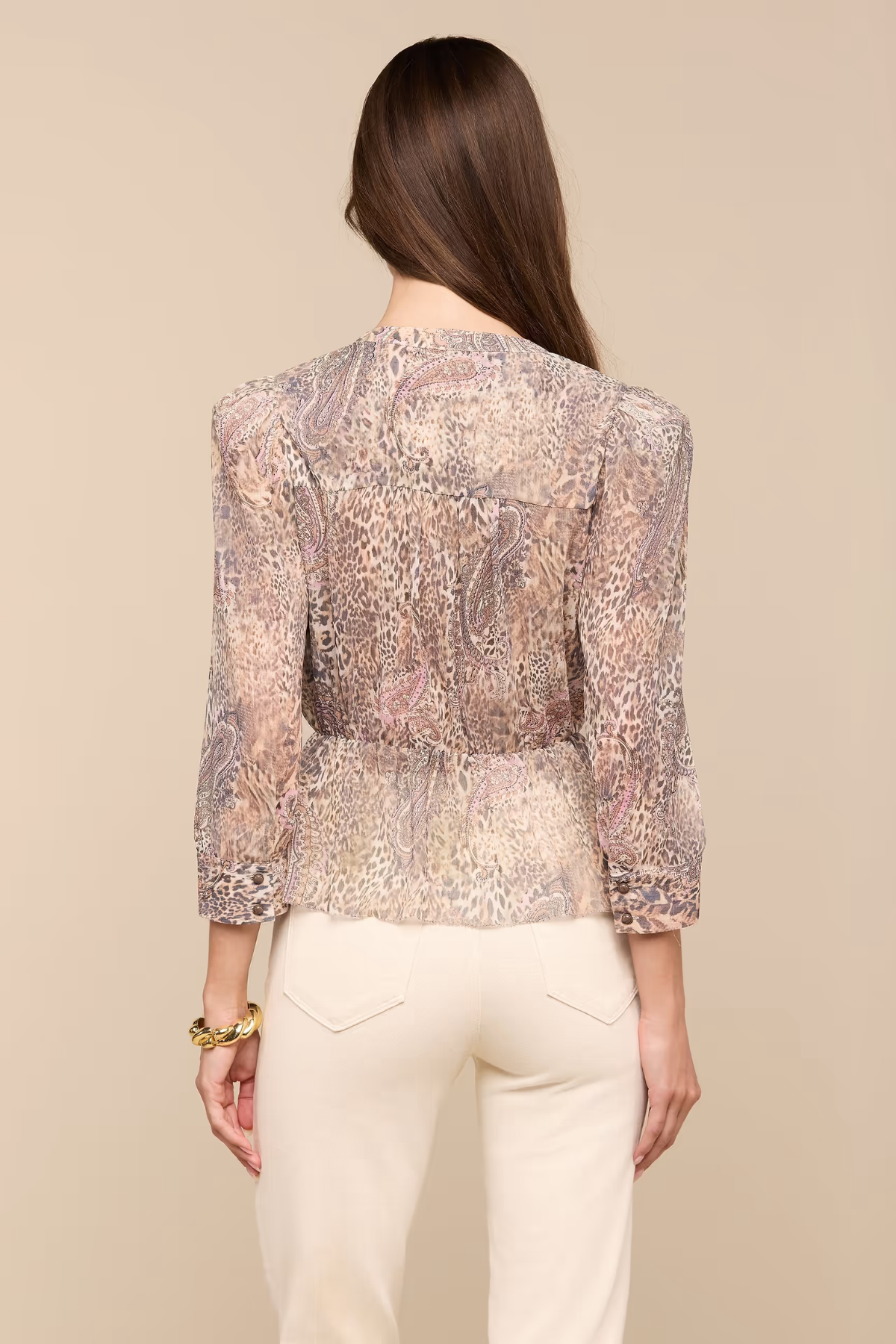 Woman wearing a patterned blouse and white pants on a beige background
