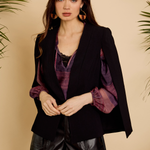Woman wearing a black blazer with purple accents and leather shorts against a beige background