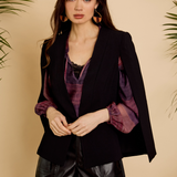 Woman wearing a black blazer with purple accents and leather shorts against a beige background