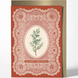 A vintage-style holiday greeting card with a terracotta red border, white lace-like ornamental pattern, and a central cream oval featuring a green pine branch. The card reads 'SEASONS GREETINGS' and is shown standing upright with a metallic gold envelope behind it on a light gray background.