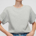 Woman wearing a gray t-shirt and blue jeans against a plain background