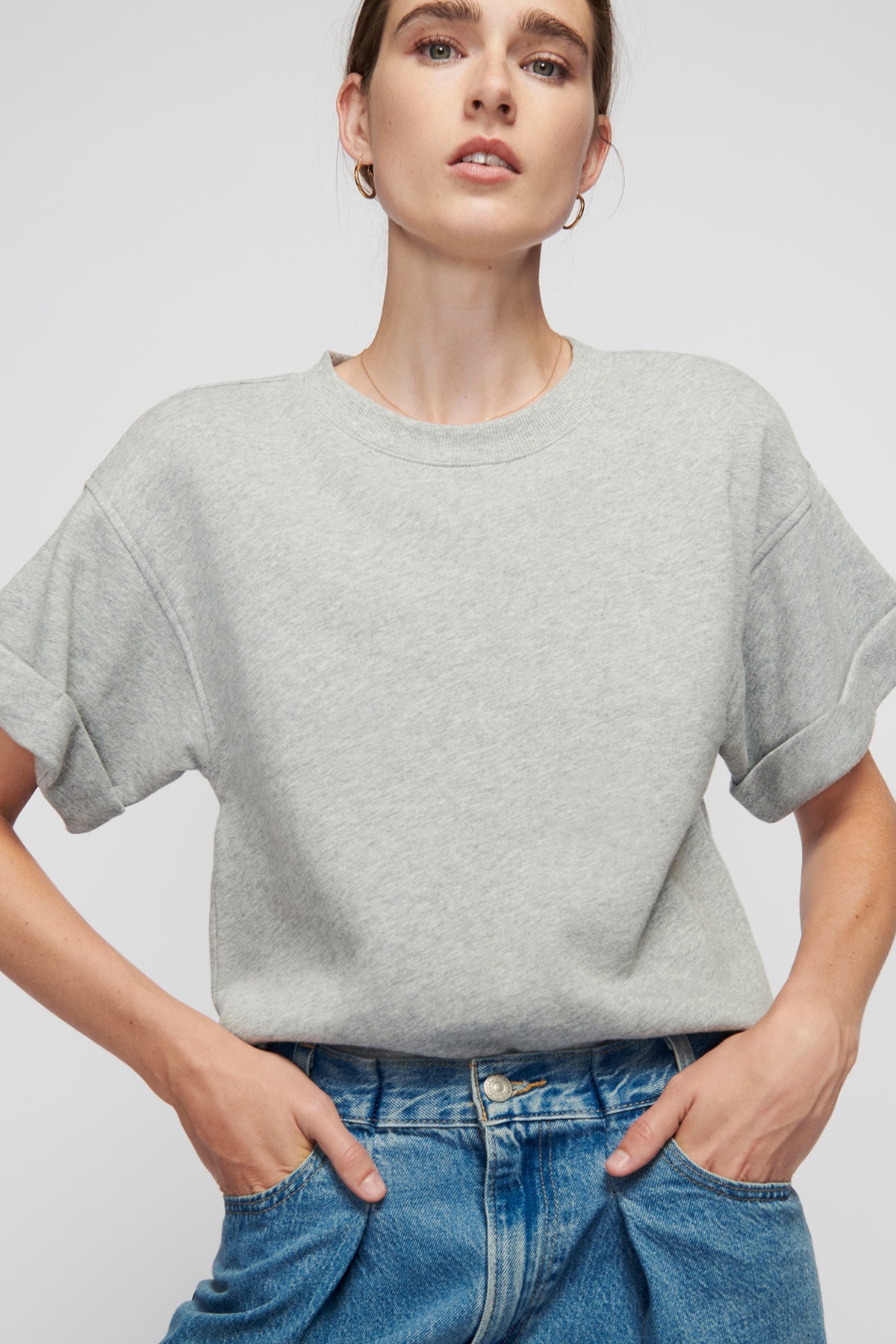 Woman wearing a gray t-shirt and blue jeans against a plain background