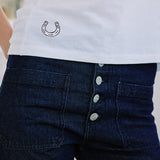White shirt with embroidered horseshoe design and dark blue jeans with silver buttons.