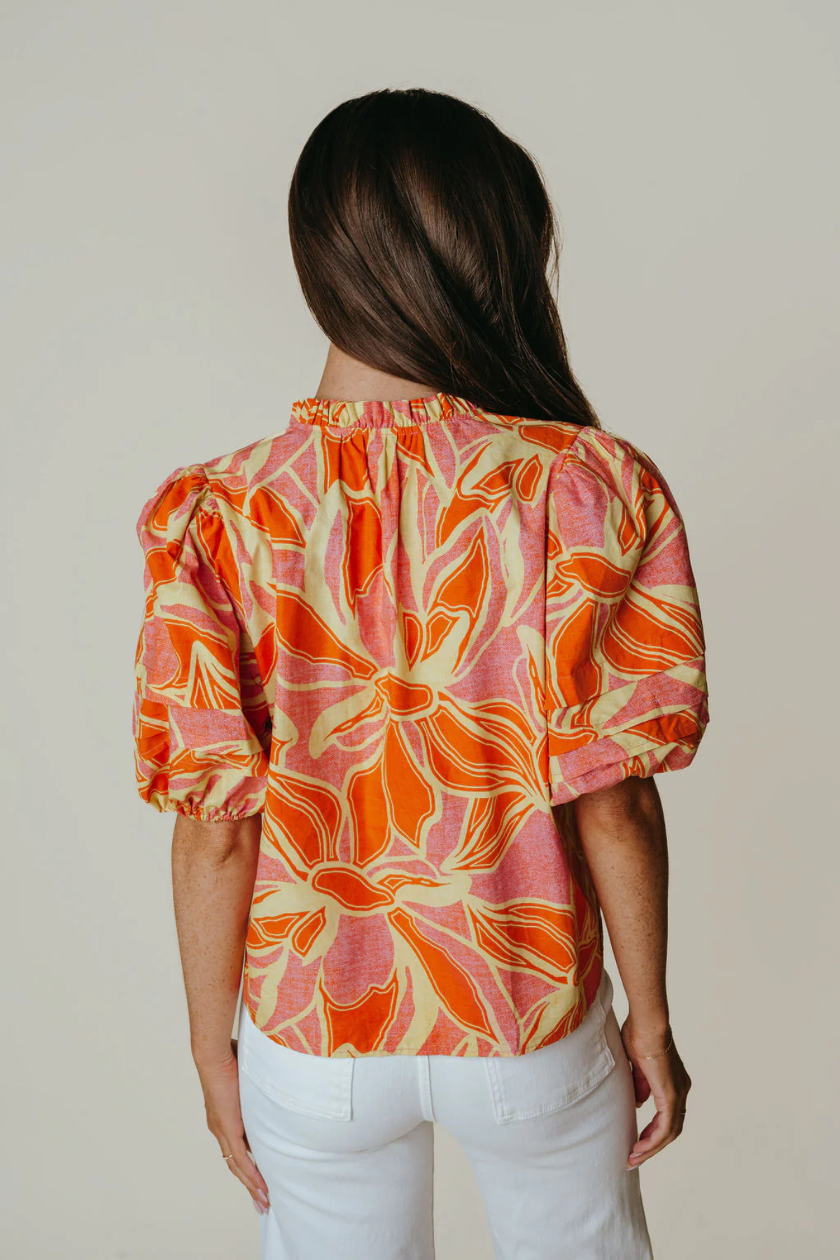 Woman wearing a colorful floral blouse with white pants against a plain background