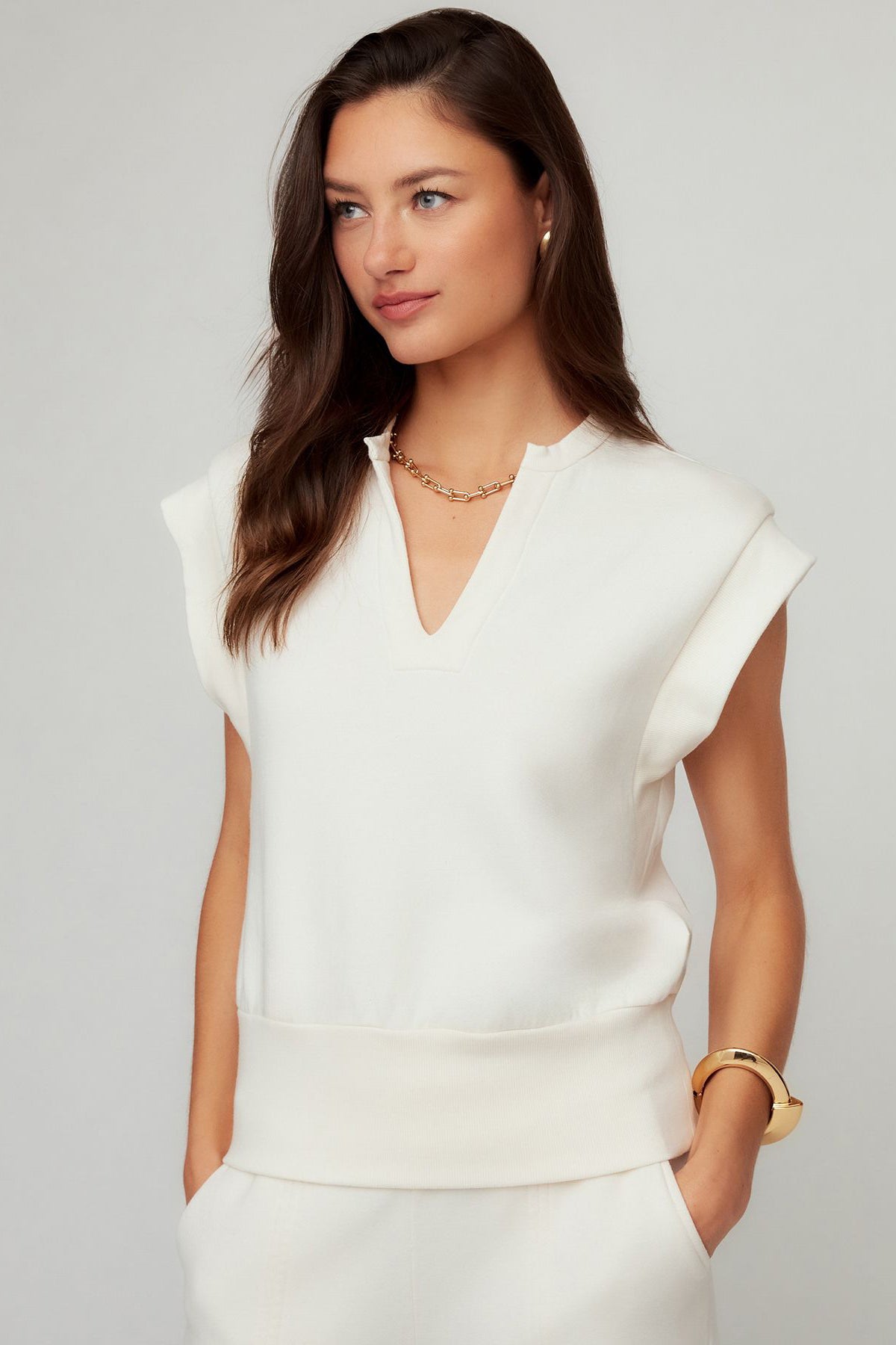 Woman wearing a white sleeveless top and pants against a gray background