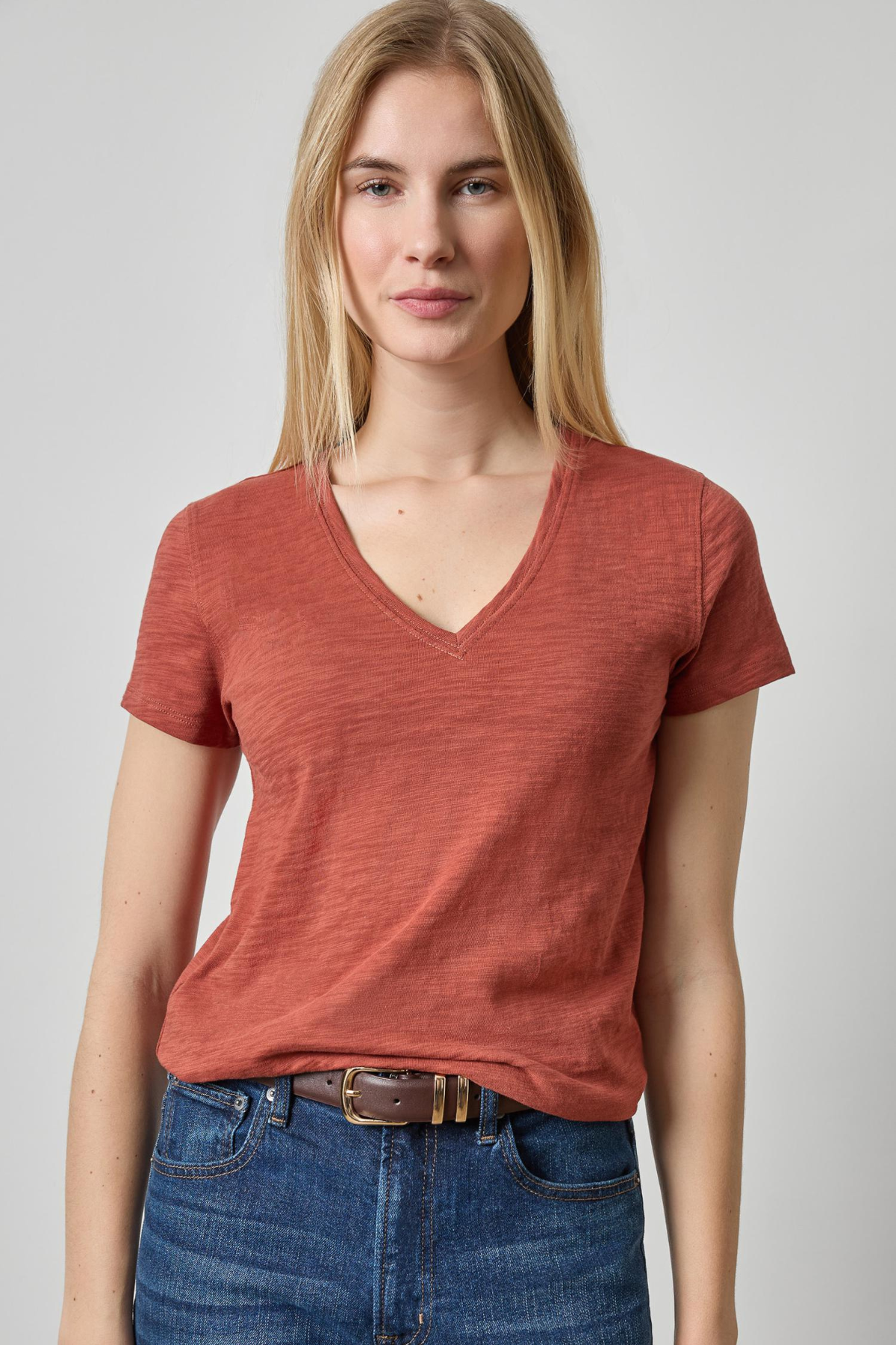 Woman wearing a red t-shirt and blue jeans on a plain background
