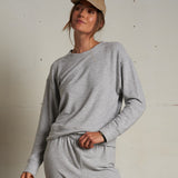 Woman wearing a light grey long-sleeve knit top with a relaxed fit, photographed against a soft neutral backdrop.