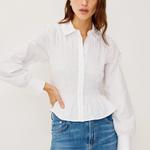 Woman wearing a white blouse and blue jeans against a plain background