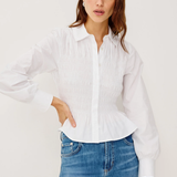 Woman wearing a white blouse and blue jeans against a plain background