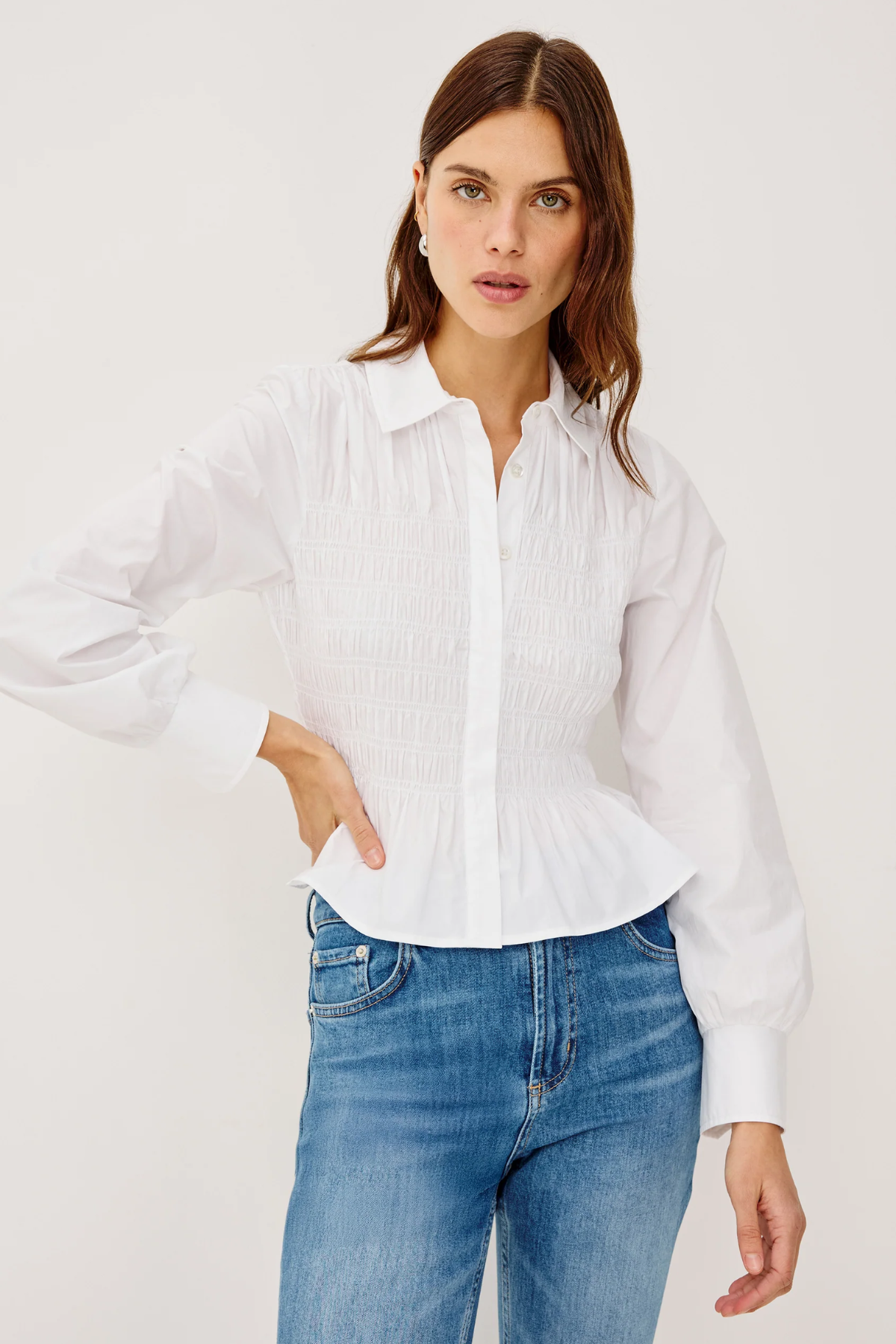 Woman wearing a white blouse and blue jeans against a plain background