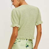 Woman wearing a light green textured top and floral skirt against a white background