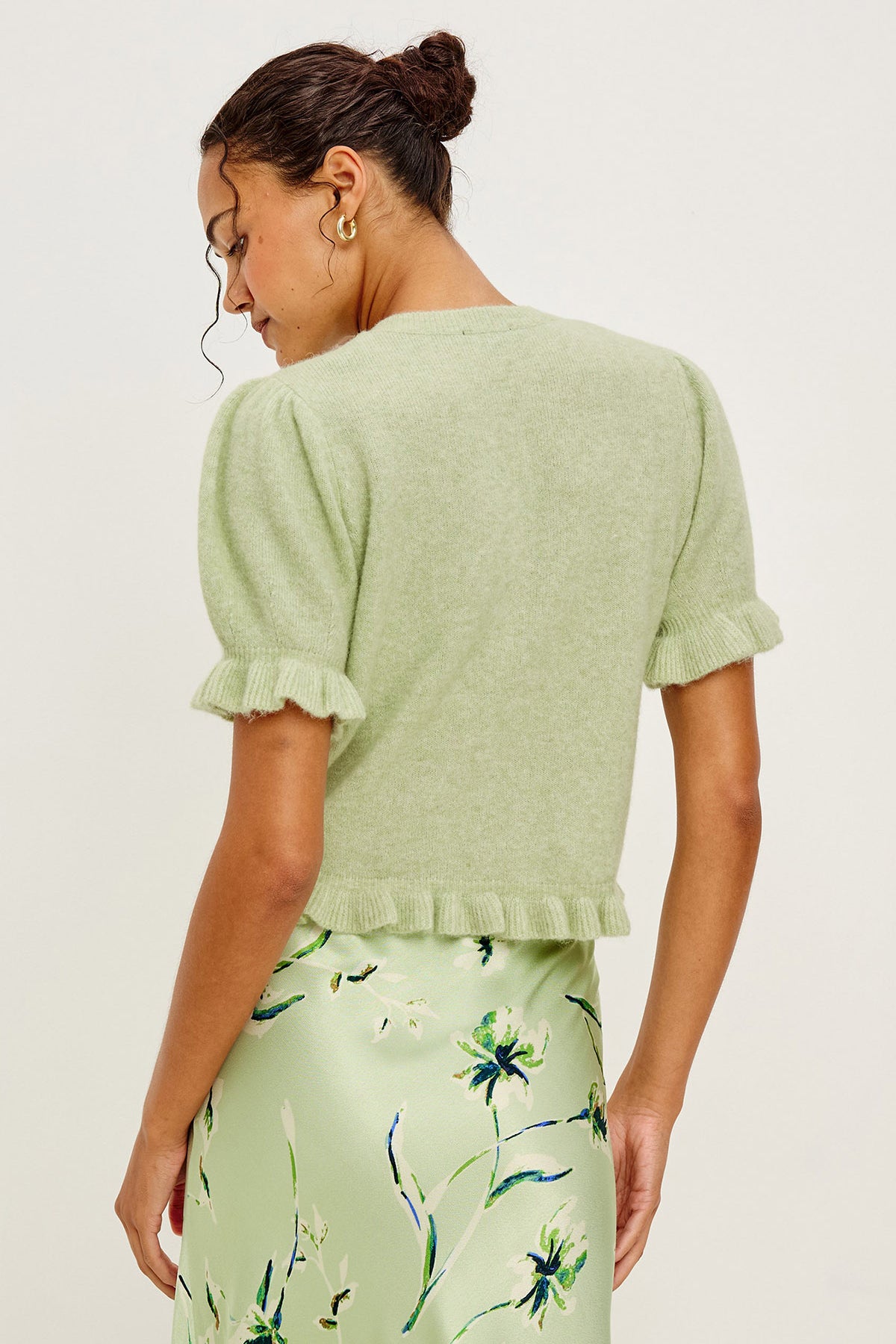 Woman wearing a light green textured top and floral skirt against a white background