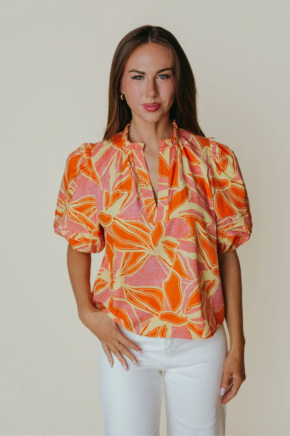 Woman wearing a colorful patterned blouse with white pants against a plain background