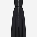A black sleeveless midi dress with thin shoulder straps, a front zipper, a matching black belt with a silver buckle, and a tiered skirt, shown against a light gray background.