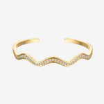 A gold wavy open cuff bracelet adorned with small clear pavé stones along the front curve, shown on a light gray background.