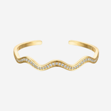 A gold wavy open cuff bracelet adorned with small clear pavé stones along the front curve, shown on a light gray background.