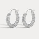 Gold pavé huggie earrings displayed against a warm neutral background