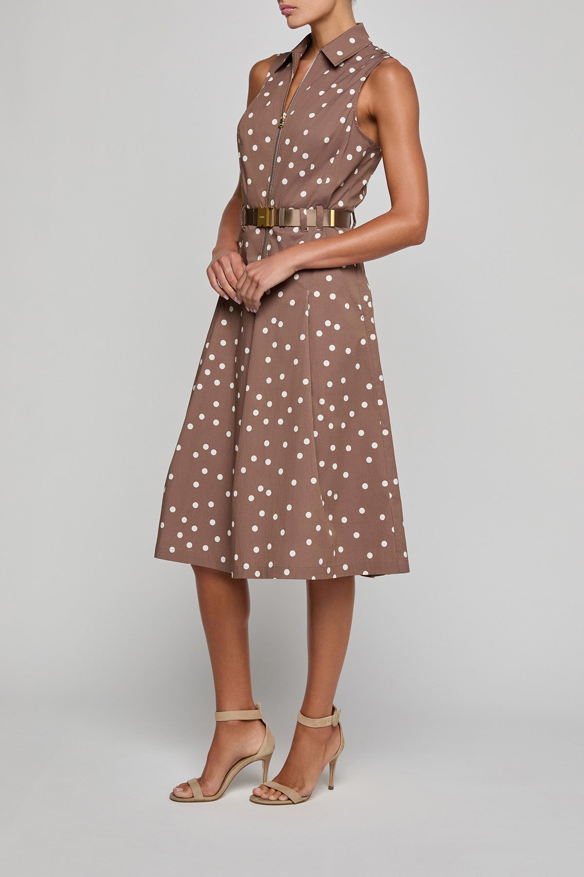 Woman wearing a brown polka dot dress with a belt on a gray background