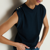 Woman wearing a dark blue sleeveless top with button details and blue jeans against a plain background