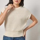 Woman wearing a cream ribbed sweater and blue jeans against a plain background