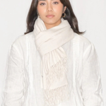 A woman wearing a light cream-colored scarf with fringe detailing and a matching white textured top, photographed against a plain white background.