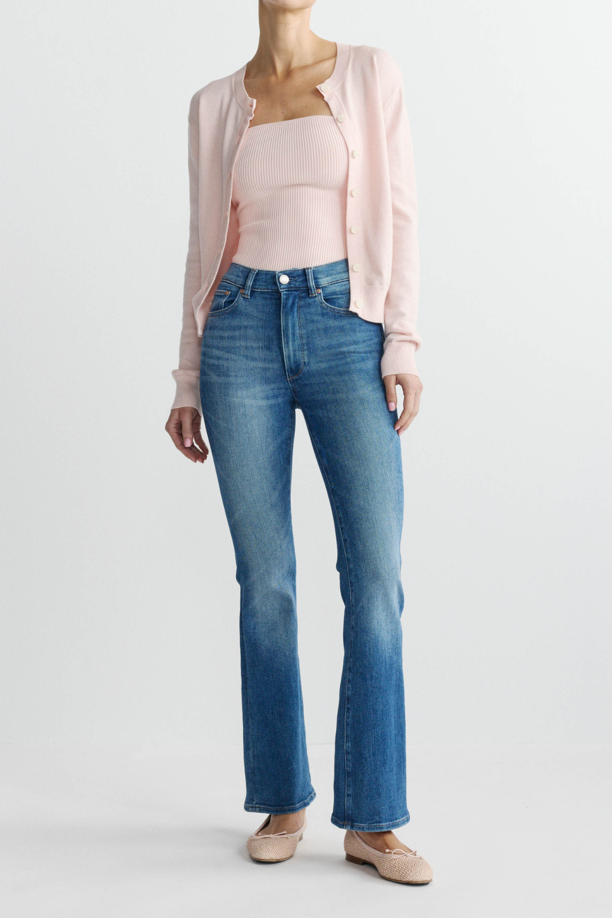 Person wearing a light pink cardigan, white top, and blue jeans on a white background