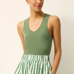 Woman wearing a green sleeveless top and green and white striped pants on a beige background