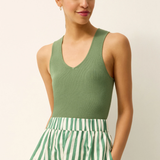 Woman wearing a green sleeveless top and green and white striped pants on a beige background