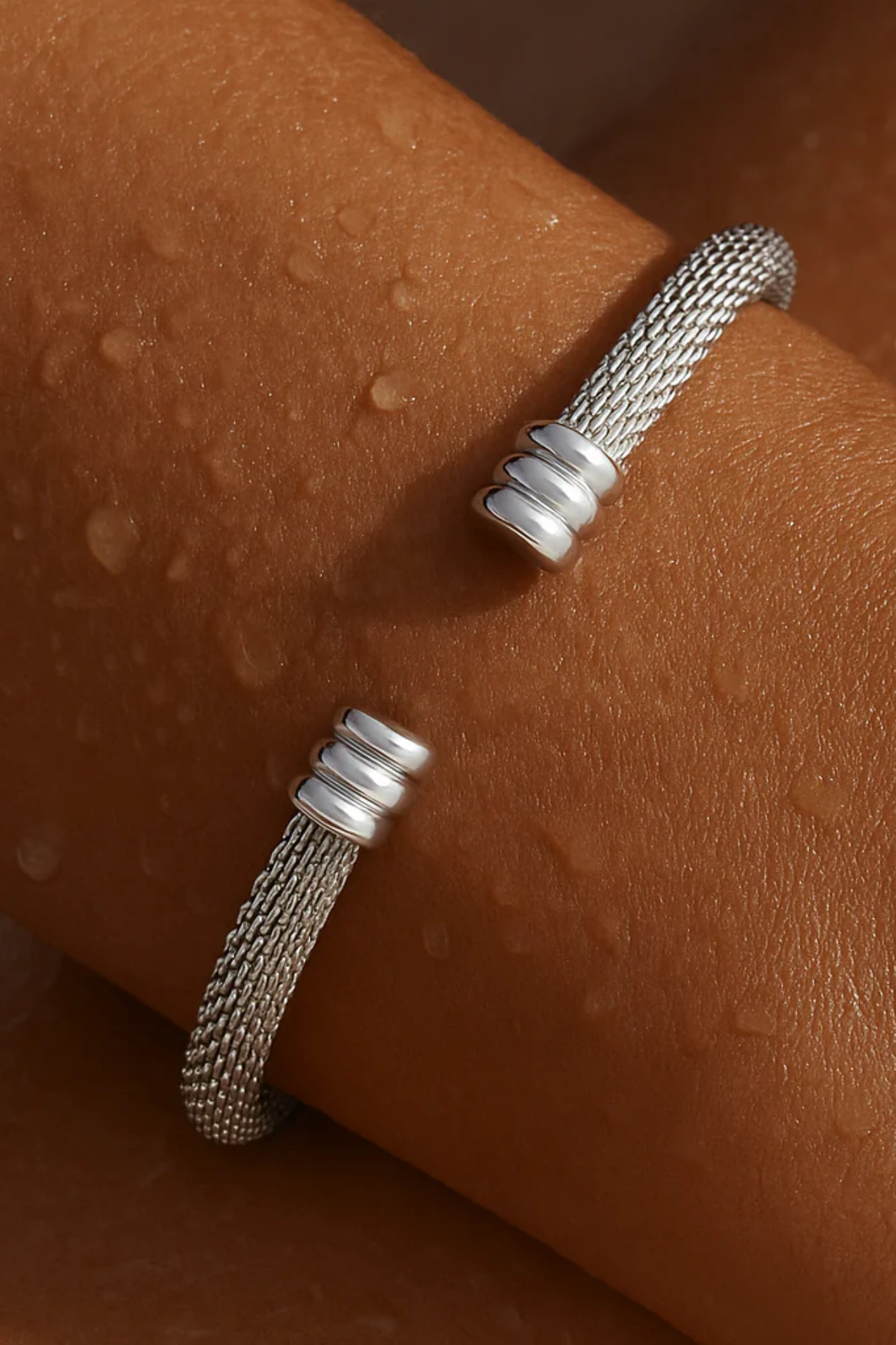 Silver textured bracelet on a person's wrist against a brown background