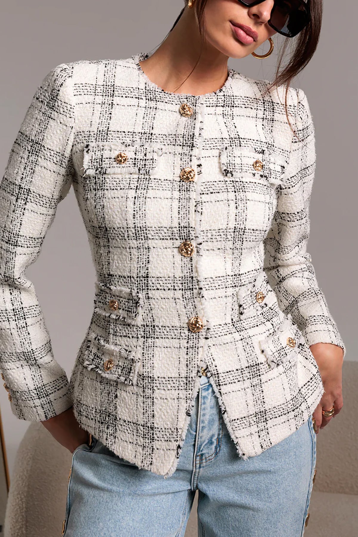 Woman wearing a checkered blazer with gold buttons against a neutral background