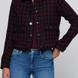 A cropped, long-sleeve plaid jacket in dark red and black tweed, worn by a model with blue jeans against a light gray studio background.
