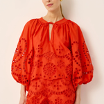 Woman wearing a red embroidered outfit against a beige background