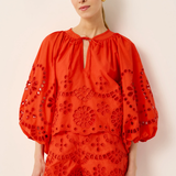 Woman wearing a red embroidered outfit against a beige background