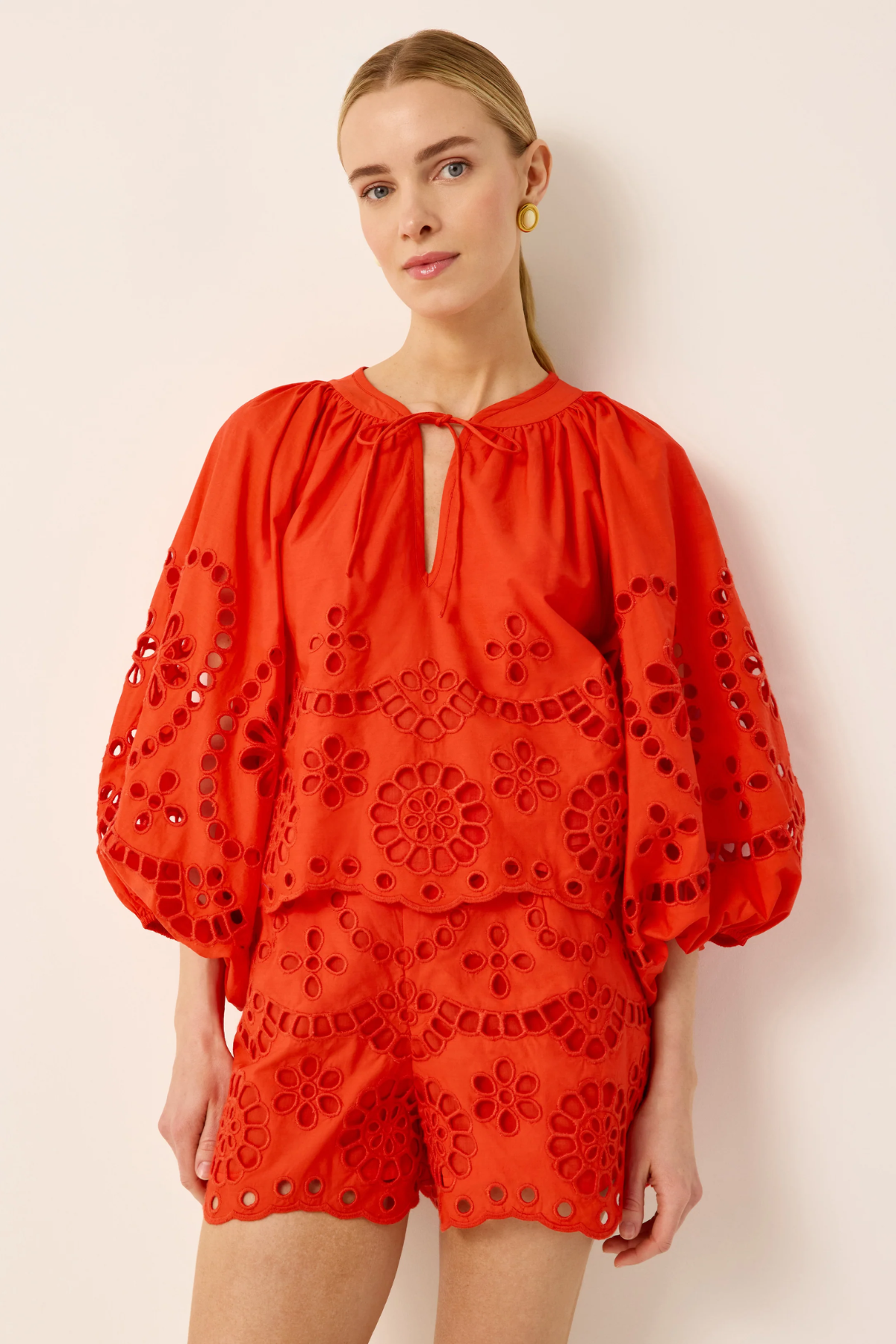 Woman wearing a red embroidered outfit against a beige background