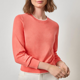 Woman wearing a coral sweater and white pants against a light gray background