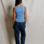 Person wearing a blue sleeveless top and dark jeans standing against a plain white background