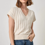 Woman wearing a beige ribbed knit top and blue jeans on a plain background