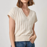 Woman wearing a beige ribbed knit top and blue jeans on a plain background