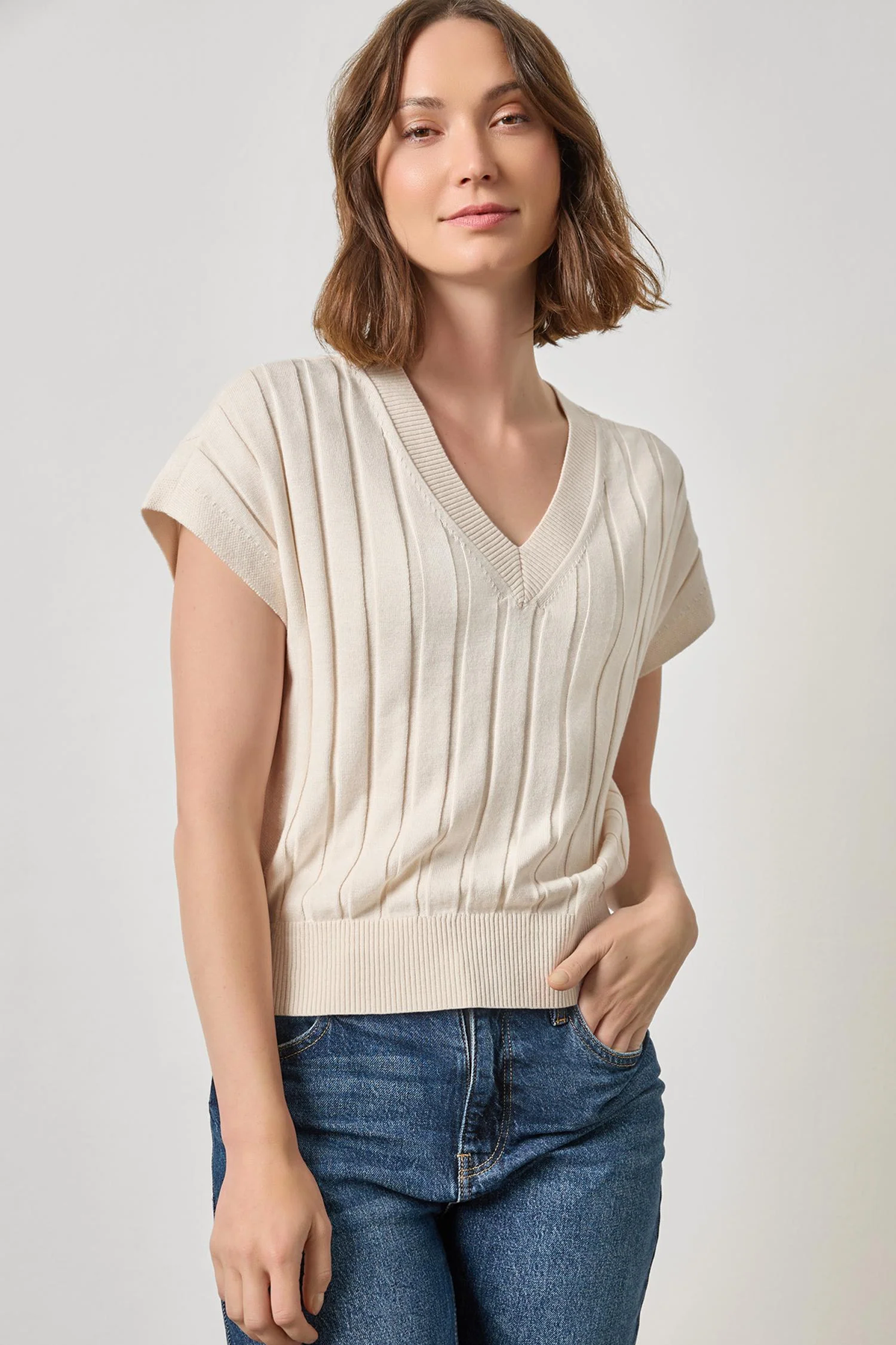 Woman wearing a beige ribbed knit top and blue jeans on a plain background