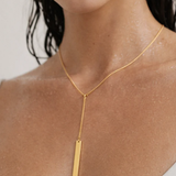 Gold necklace with a vertical pendant on a person against a neutral background
