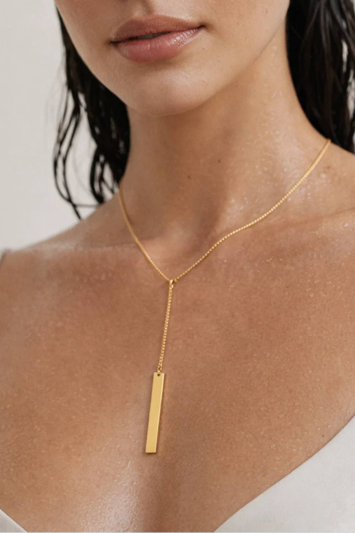 Gold necklace with a vertical pendant on a person against a neutral background