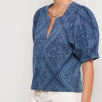 Woman wearing a blue patterned blouse with white pants on a light gray background