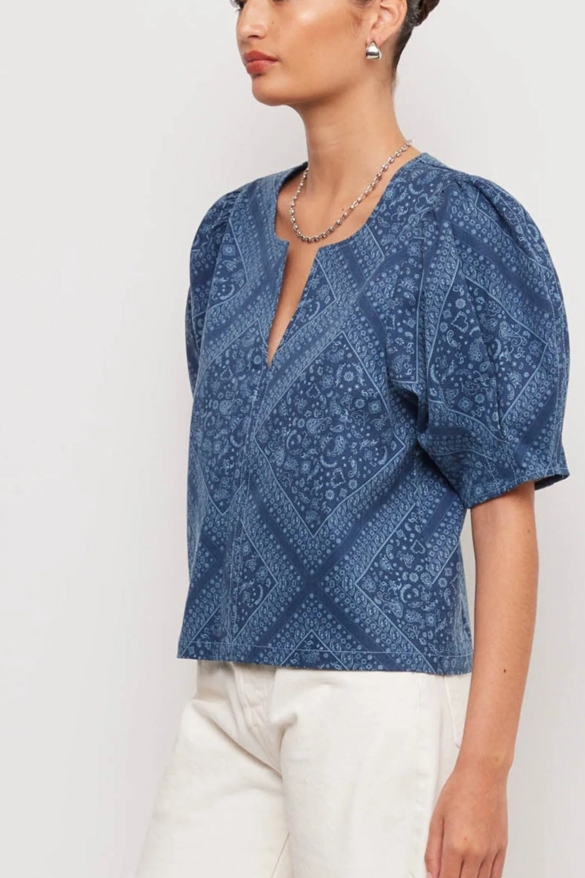 Woman wearing a blue patterned blouse with white pants on a light gray background