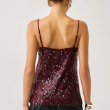 A woman shown from the back wearing a burgundy sequined camisole top with thin straps and black pants, against a plain light gray studio background.