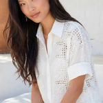 Woman wearing a white lace top and shorts sitting outdoors.